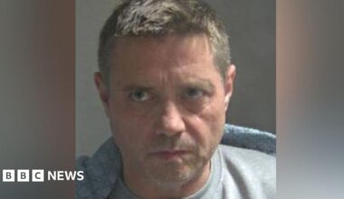 John Alford in a white shirt outside court, looking almost side-on, frowning. He is clean shaven. He has short hair, gelled into a quiff.