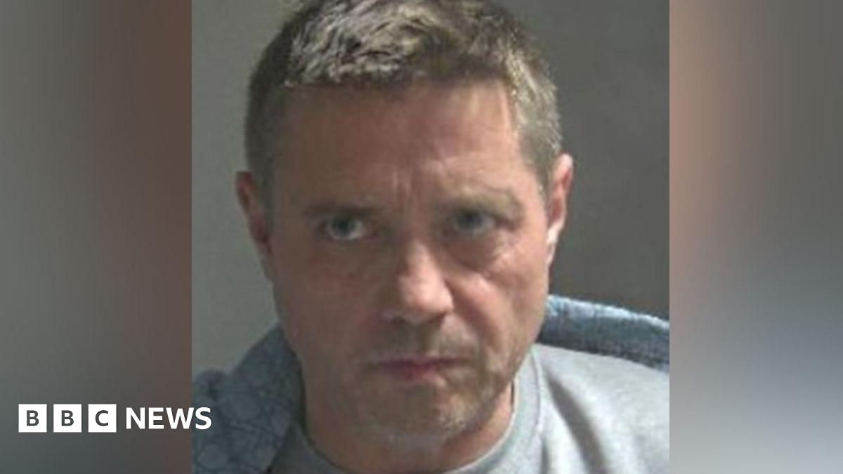 John Alford in a white shirt outside court, looking almost side-on, frowning. He is clean shaven. He has short hair, gelled into a quiff.