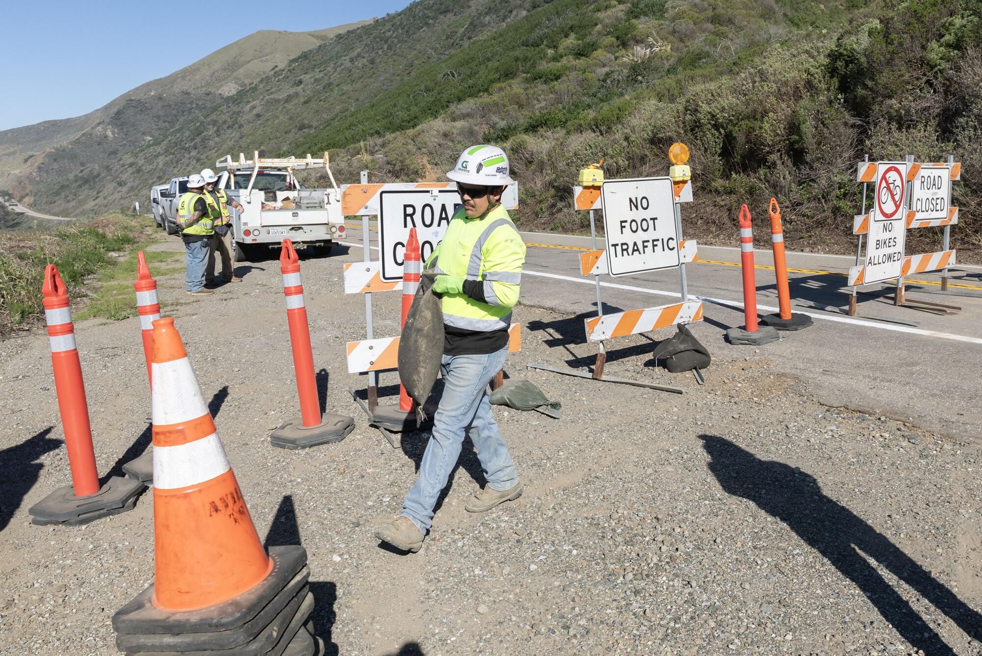 Caltrans workers remove signs indicating that California Highway 1 is closed near Lucia on Wednesday.