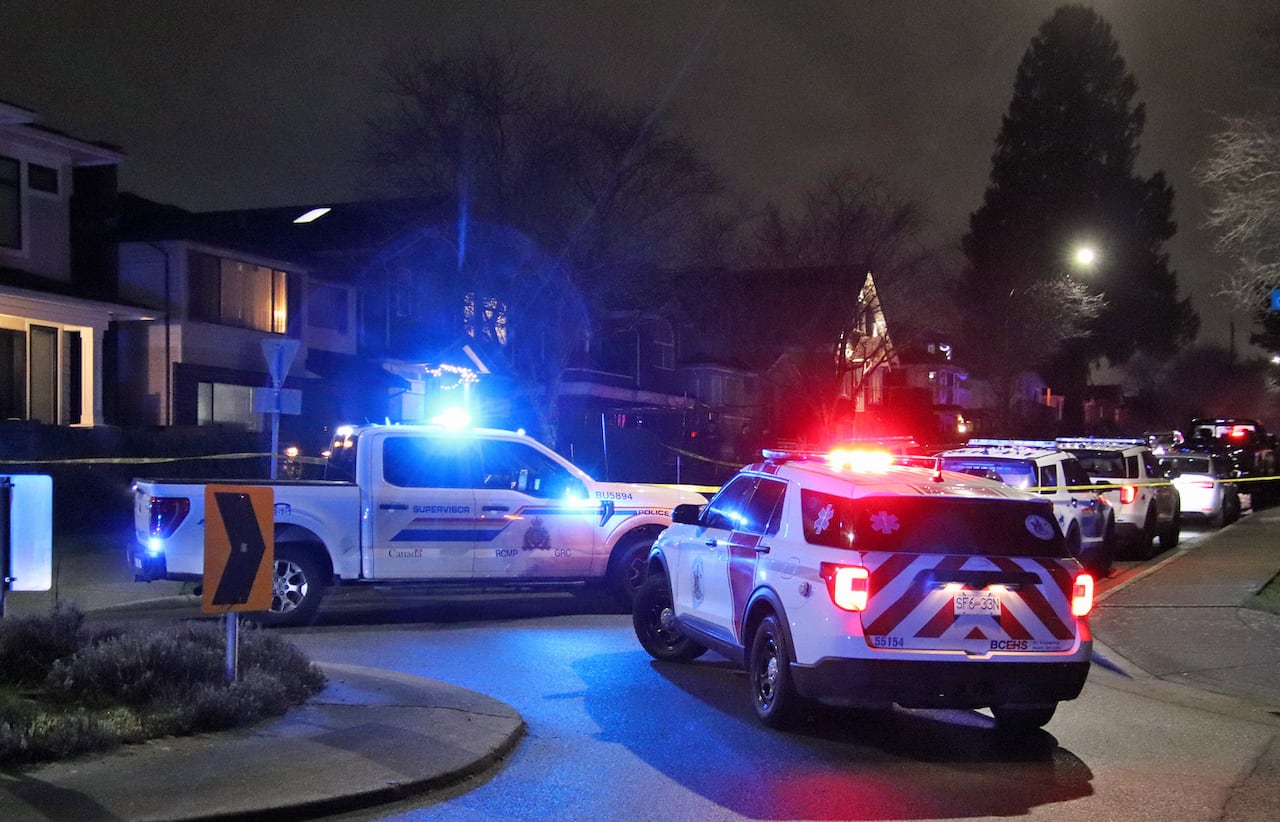 Four RCMP police cruisers are seen on a residential street with their lights on.