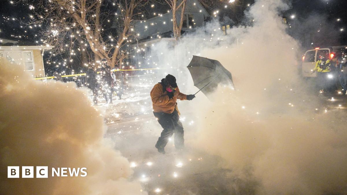 A protester on a snowy street uses an umbrella to shield themself from a cloud of tear gas and sparks in Minneapolis