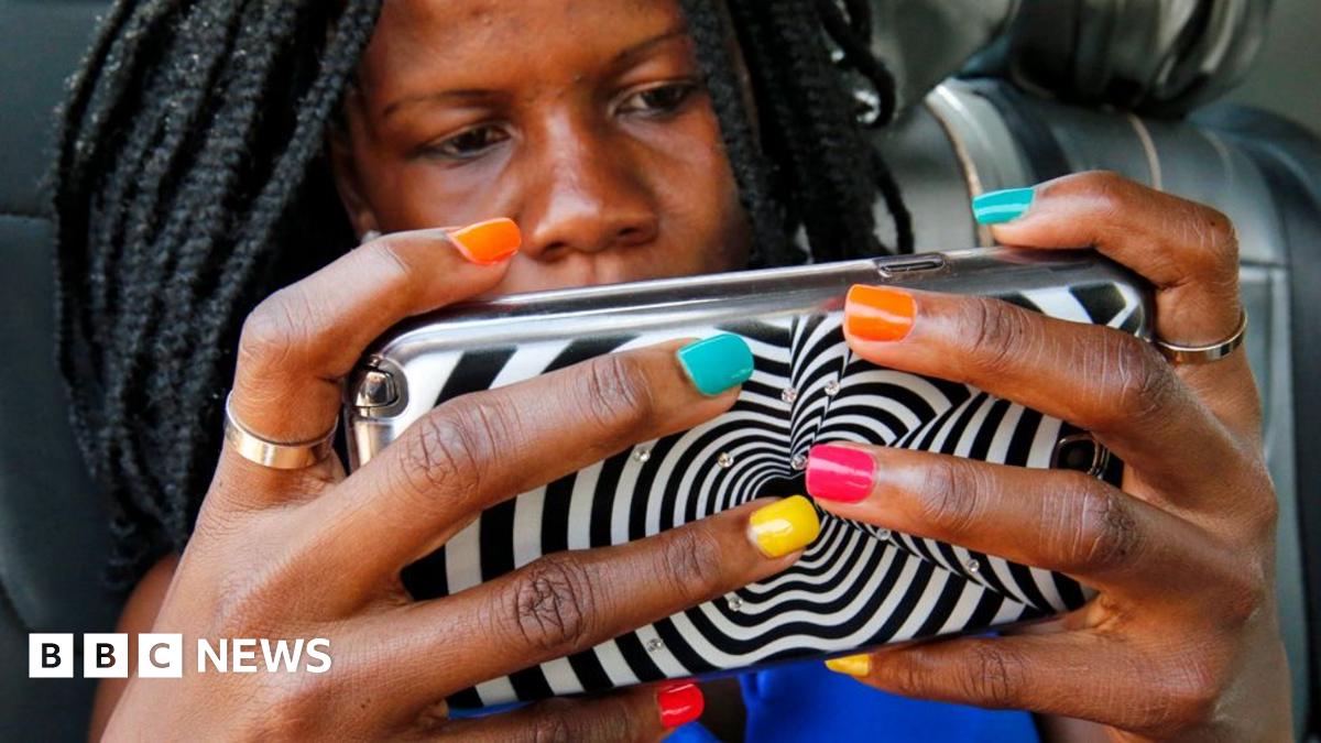 A woman with braids and multi-coloured nail varnish hold ups a mobile phone encased in a zebra design cover