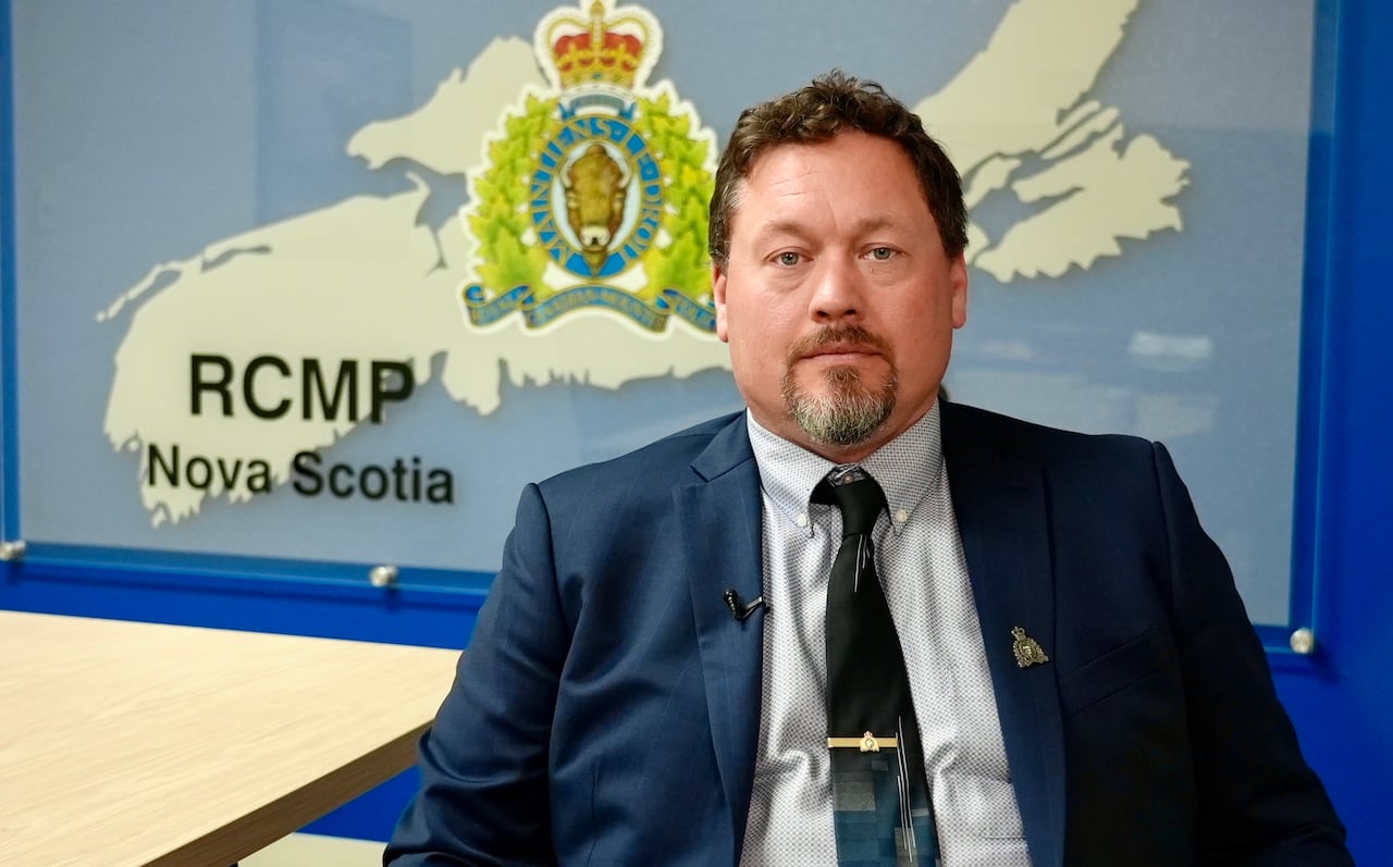 A man in a blue suit sits and smiles in front of a map of Nova Scotia.