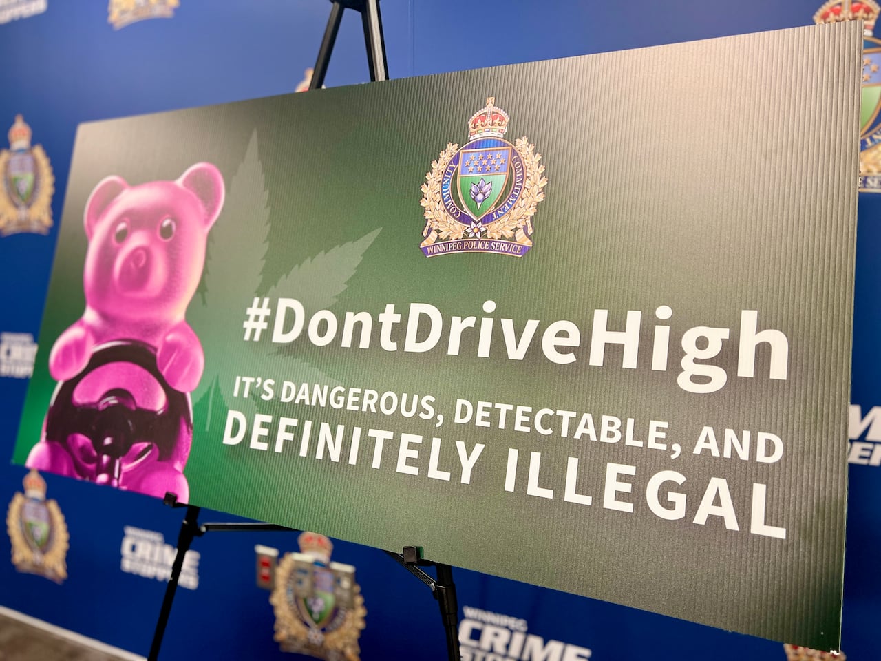 A green sign with a pink gummy bear behind a wheel and the logo of the Winnipeg police force.