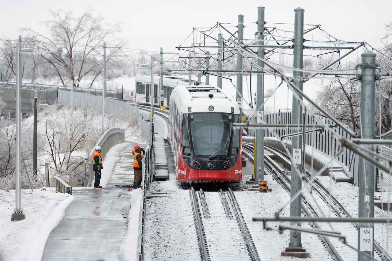 A red and white train is seen amid snow and ice as workers peer at it.