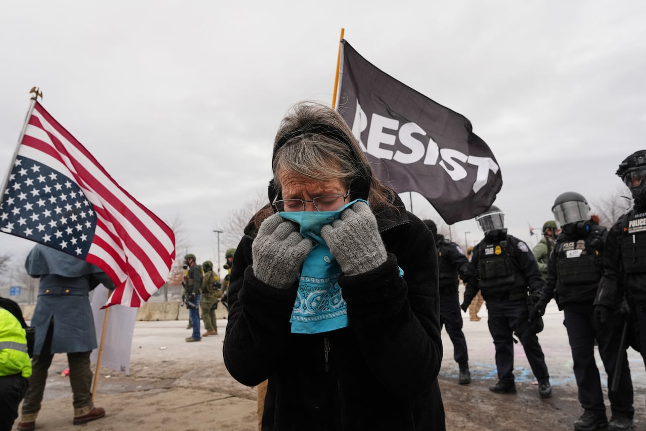 A woman, seemingly crying, covers her face with a cloth, amid protesters and police.
