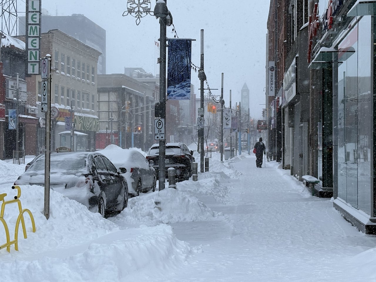 King street in Kitchener 1/15/2026. We can see down the sidewalk, there is a lot of snow everywhere and a man walking down the street in the background