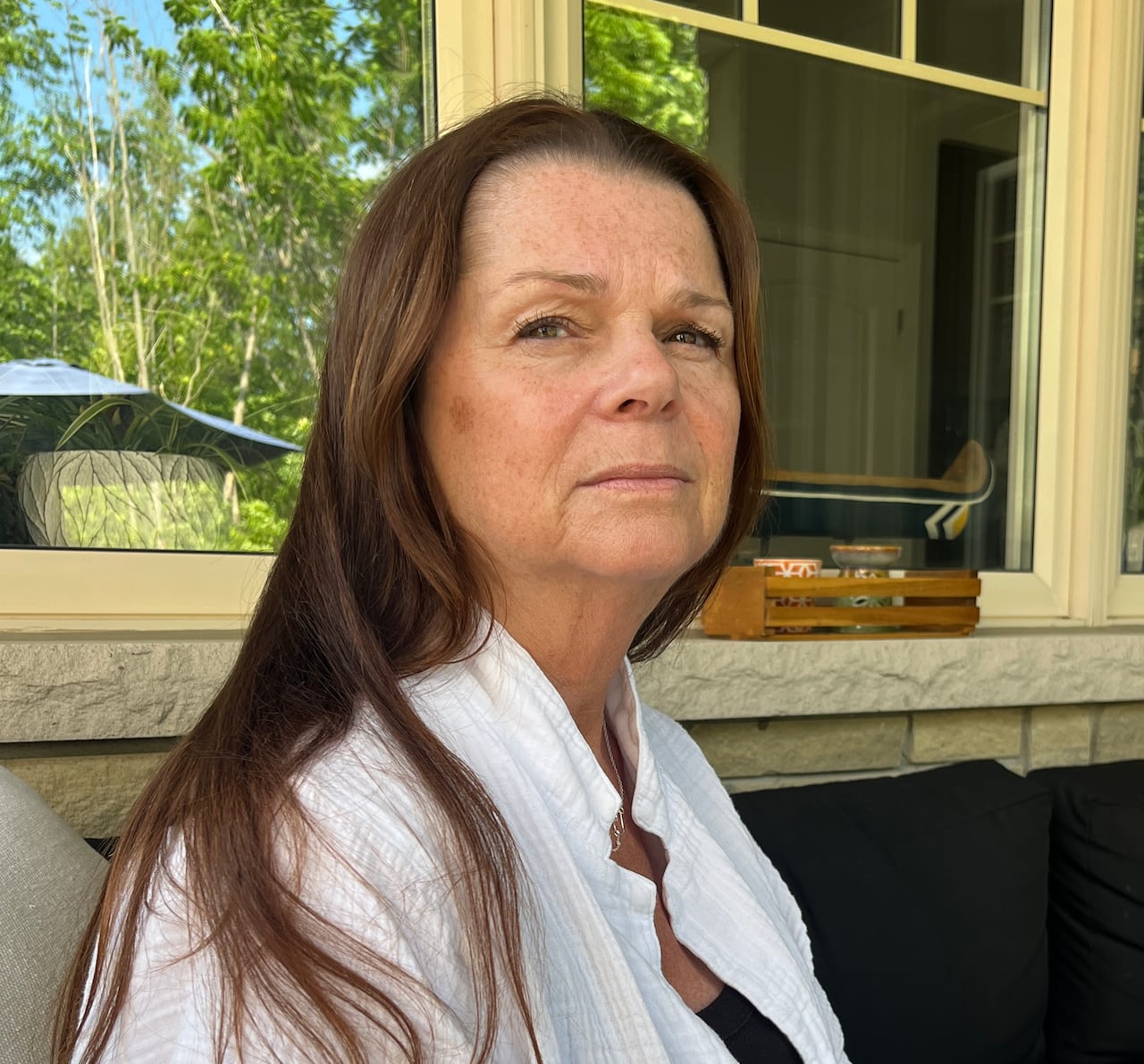 A woman with long brown hair and wearing a white short-sleeved button down shirt looks into the camera.