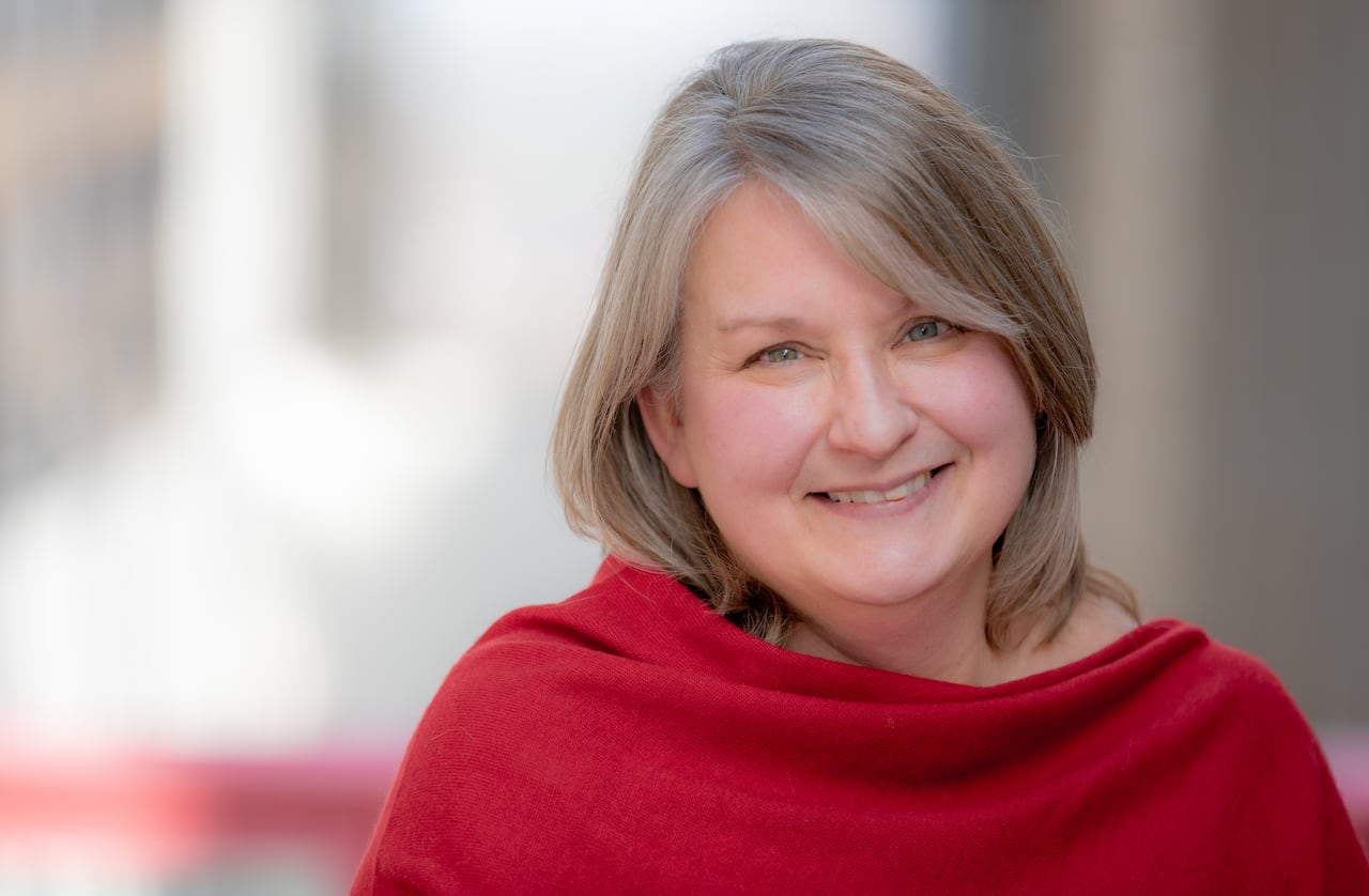 A woman with shoulder length gray hair wearing a red top smiles.