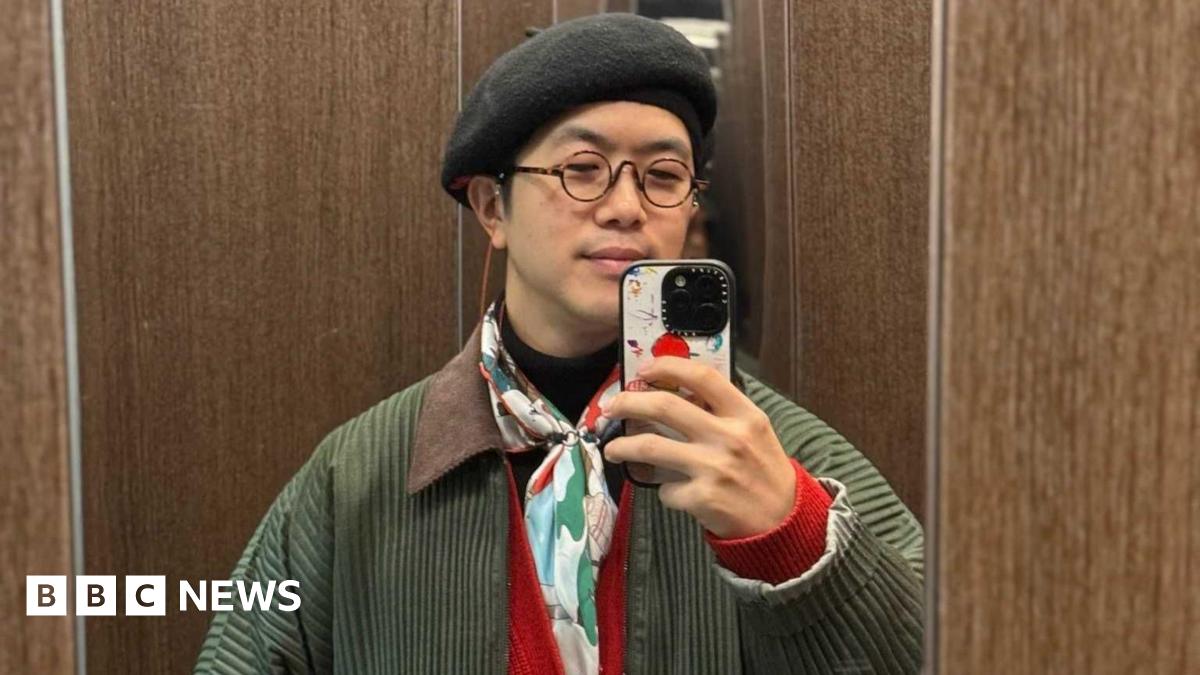 A man in a black beret and colourful scarf taking a photo in the mirror with his iPhone