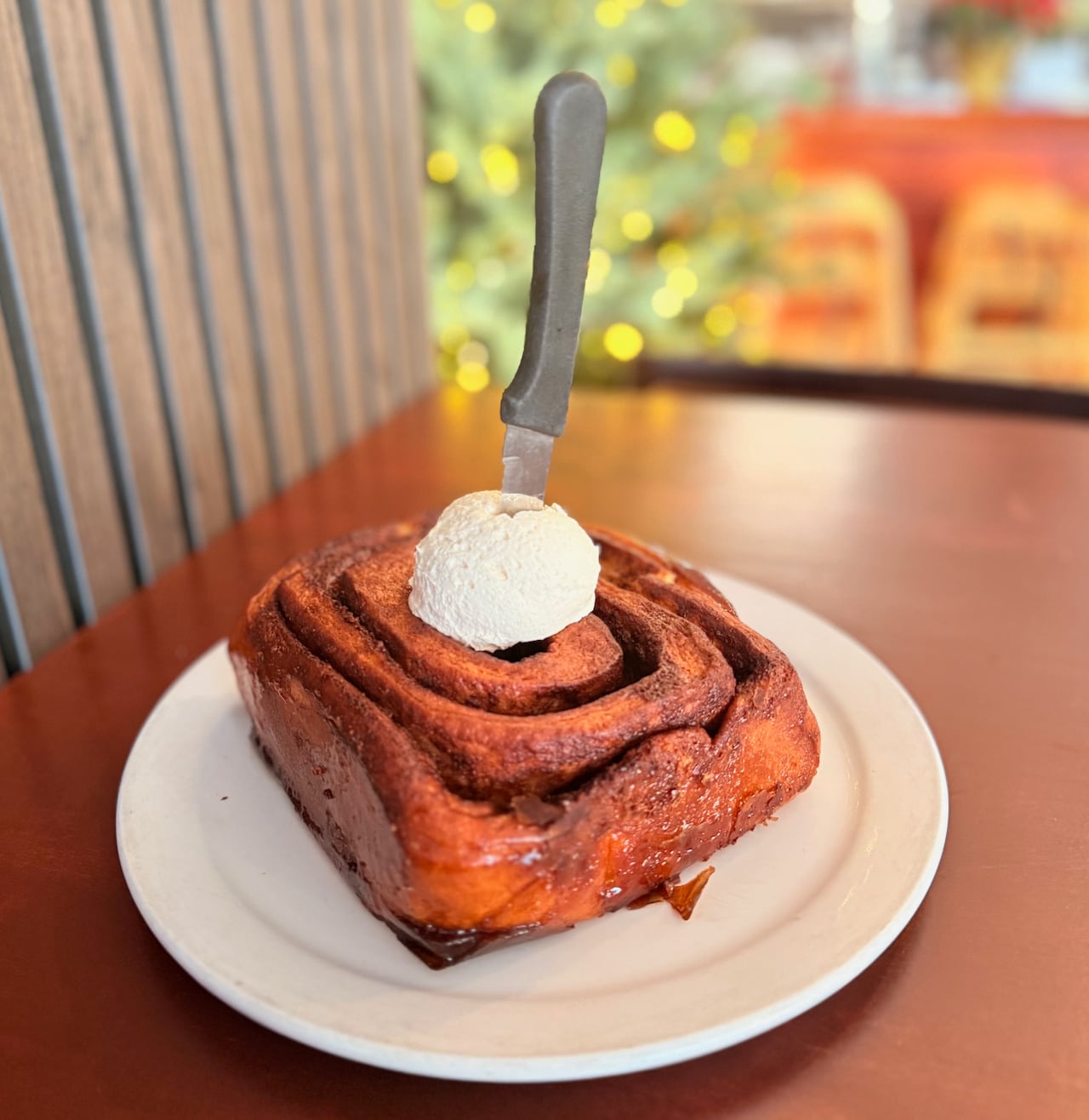 A large cinnamon bun on a plate with a dollop of icing and a knife sticking out of it