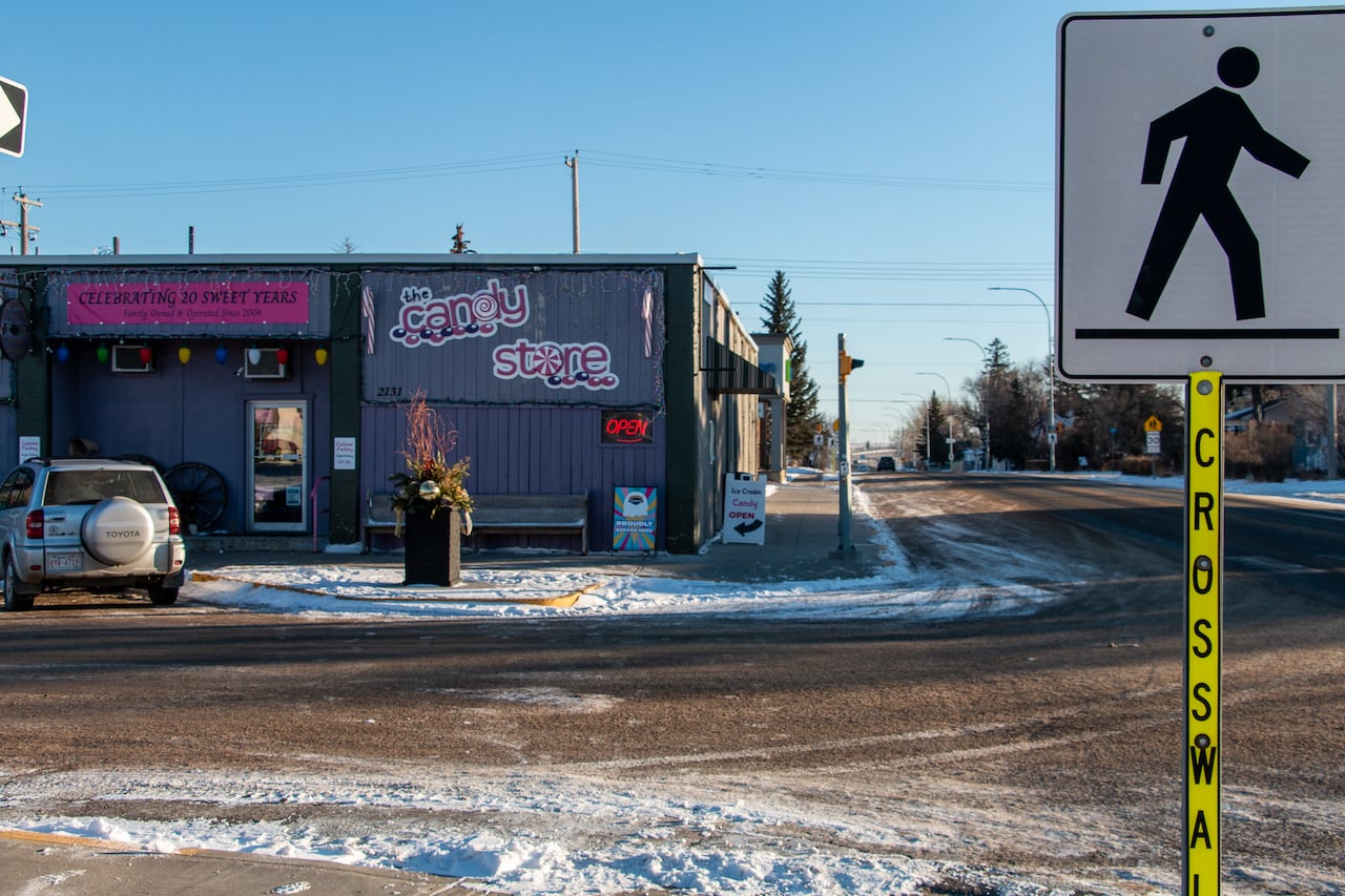 In the background, a purple building with a sign for a candy store. In the foreground, a pedestrian walk sign. 