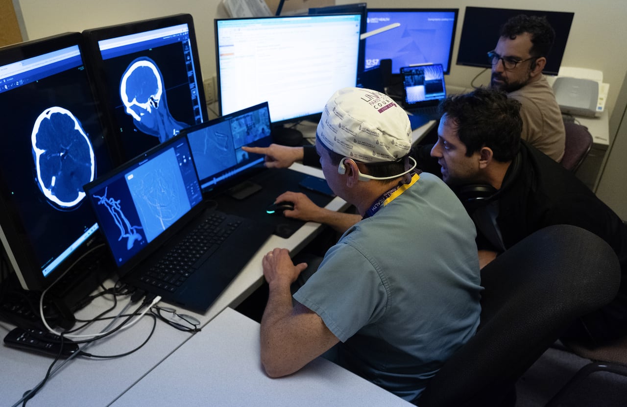 A group of people look at a handful of monitors displaying medical information.