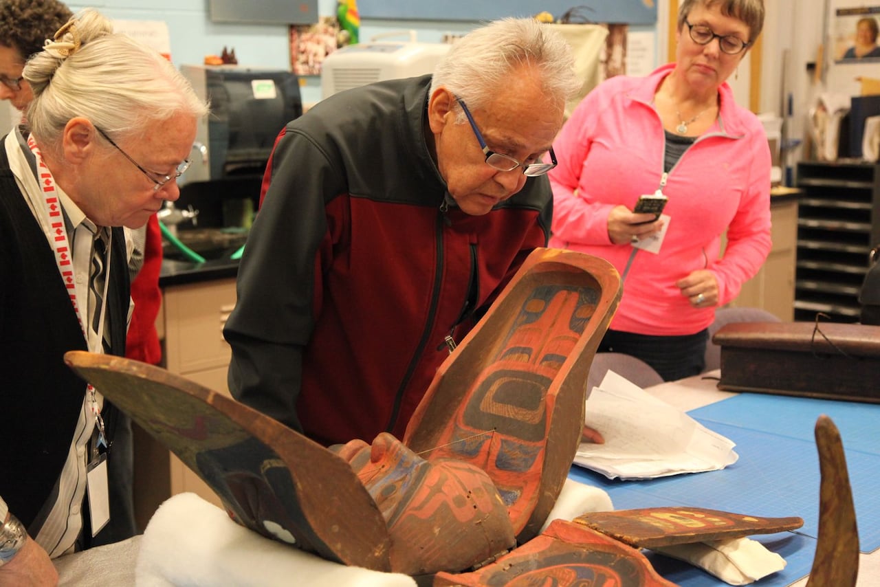 A man and woman examine a mask on a table.