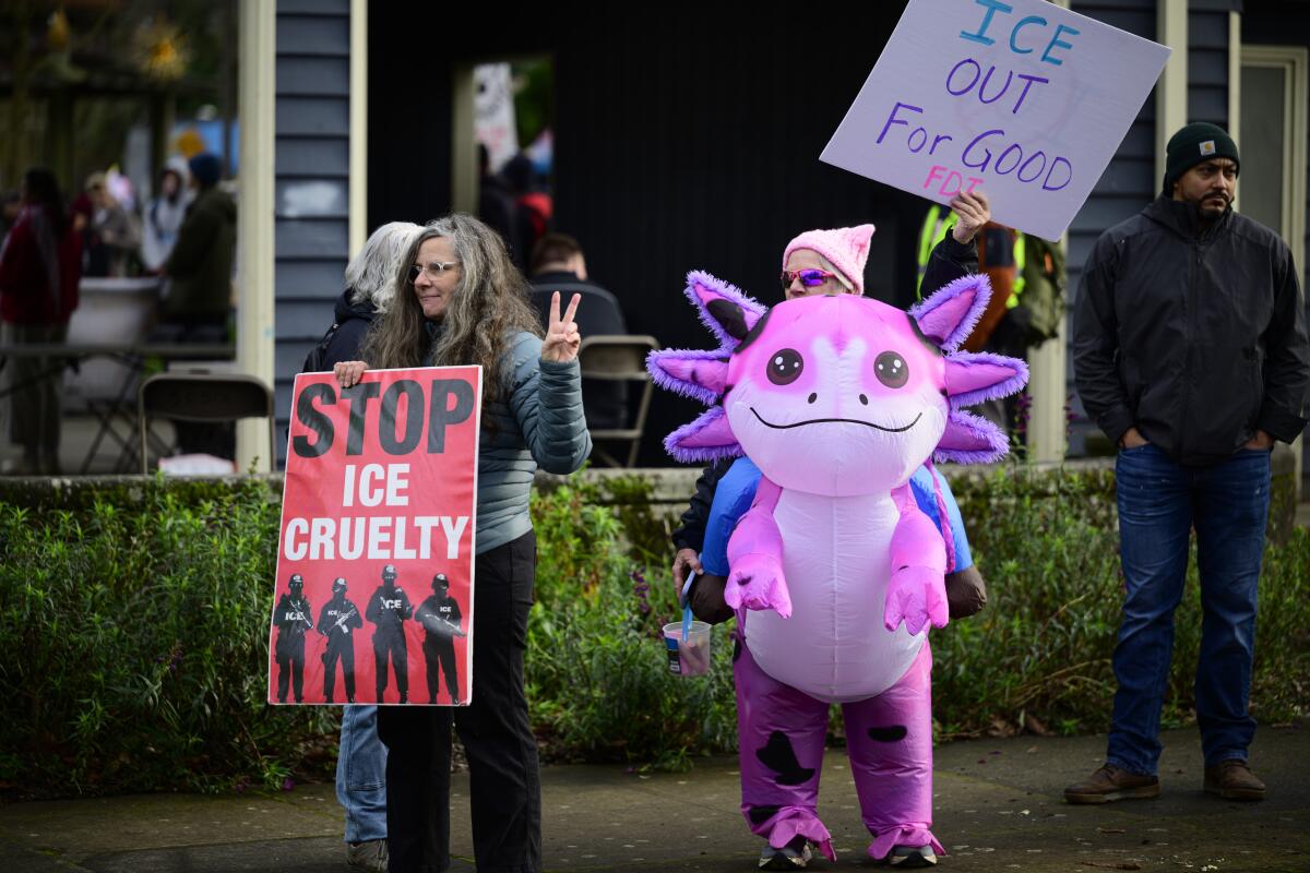 An anti-ICE activist in an inflatable costume stands next to a person with a sign during a protest