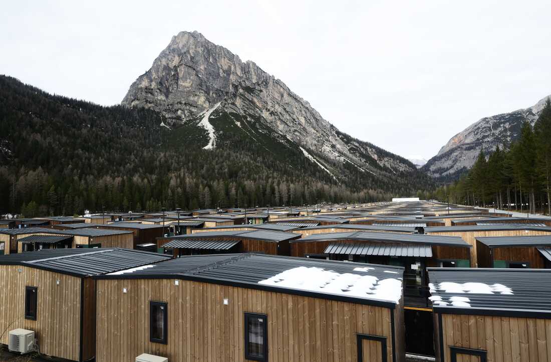 Part of the Cortina athletes village, seen in December in Fiames, near Cortina d'Ampezzo, Italy. The athletes village consists of small, one-story buildings with vertical strips of wood covering the exteriors. Tall peaks rise in the background.