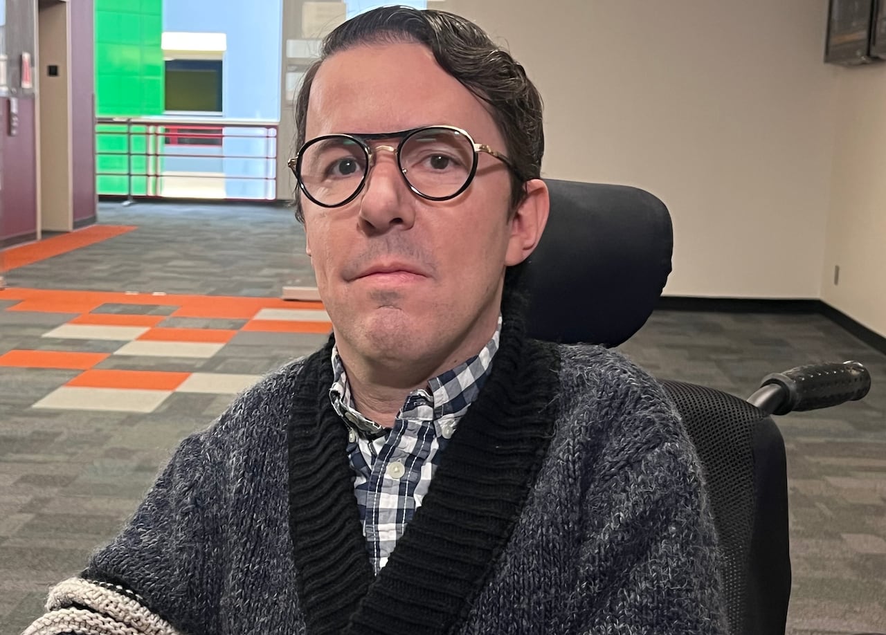 A man sits in a wheelchair, looking at the camera