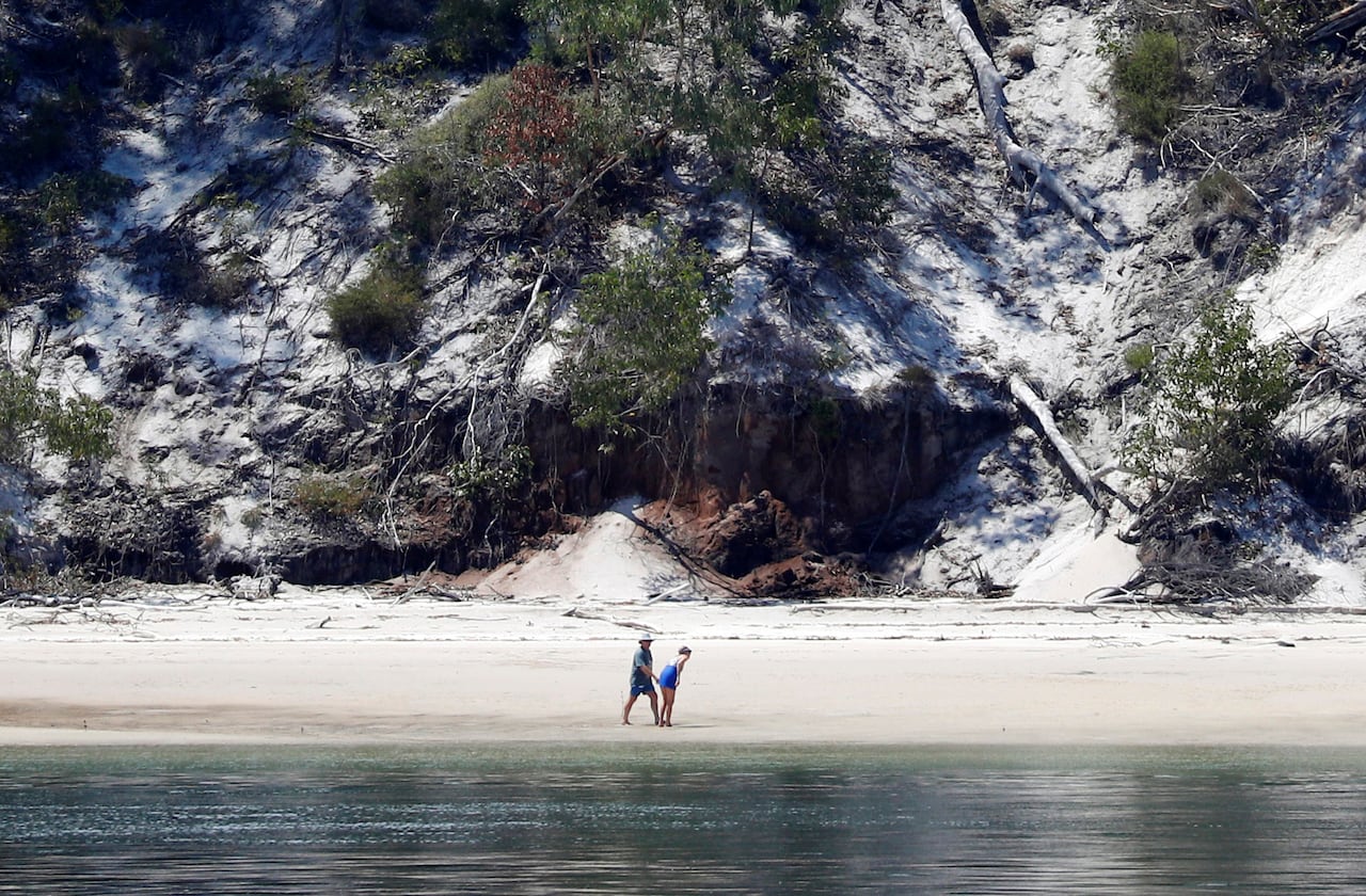 Two figures stand on a beach