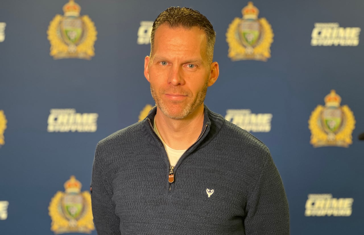 A man with blue eyes and sweater behind a sign for Winnipeg police