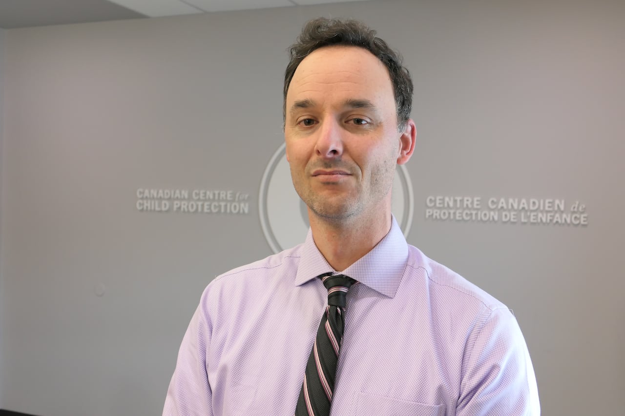 A picture of a man with brown hair behind a sign for the Canadian Center for Child Proteciton