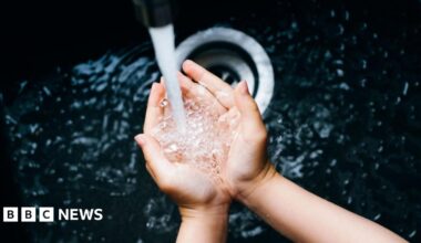 A young woman's hands cup water as it runs from a tap into a deep black sink.