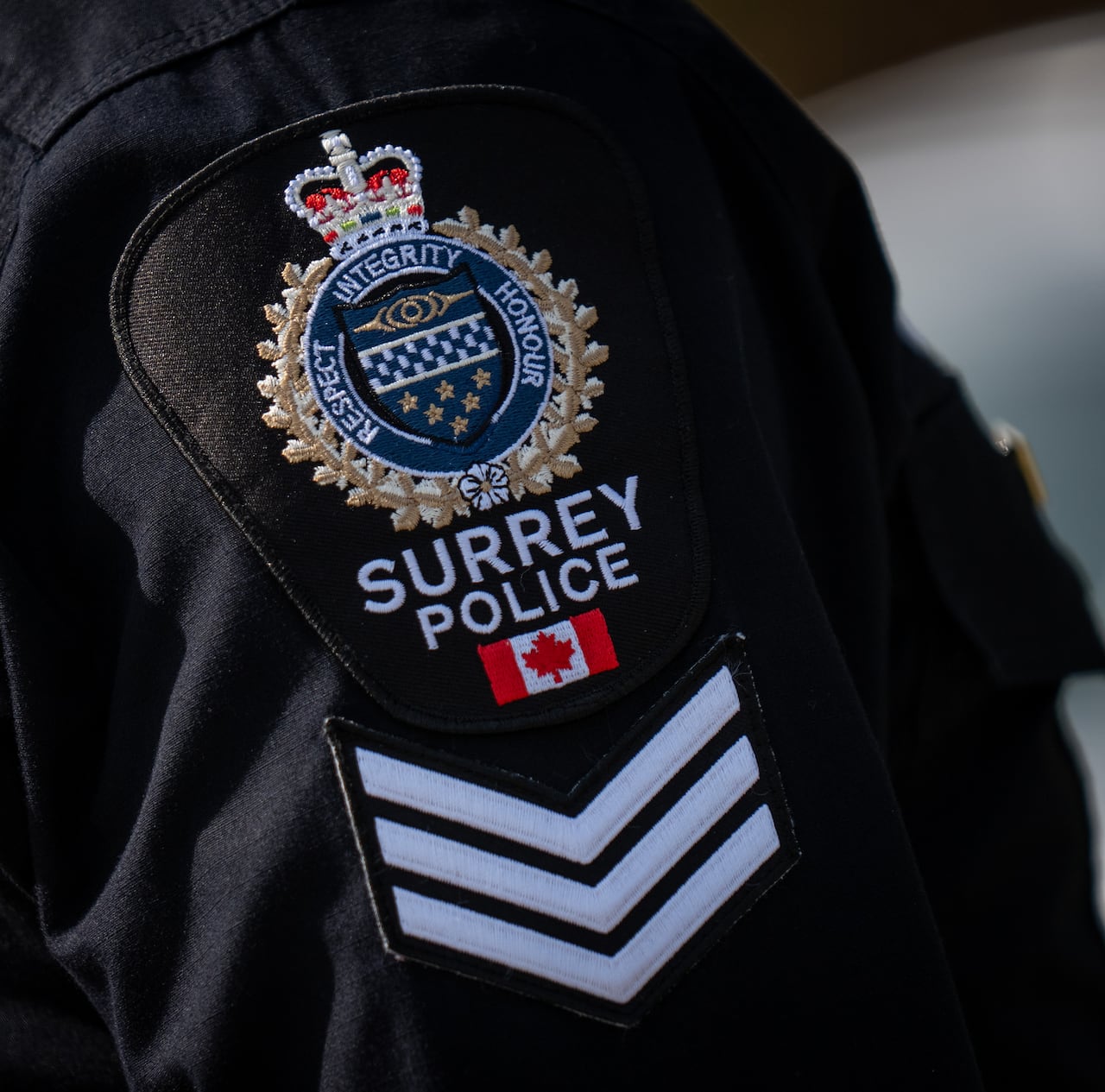 A shoulder patch on a police officer reads 'Surrey Police Service'.