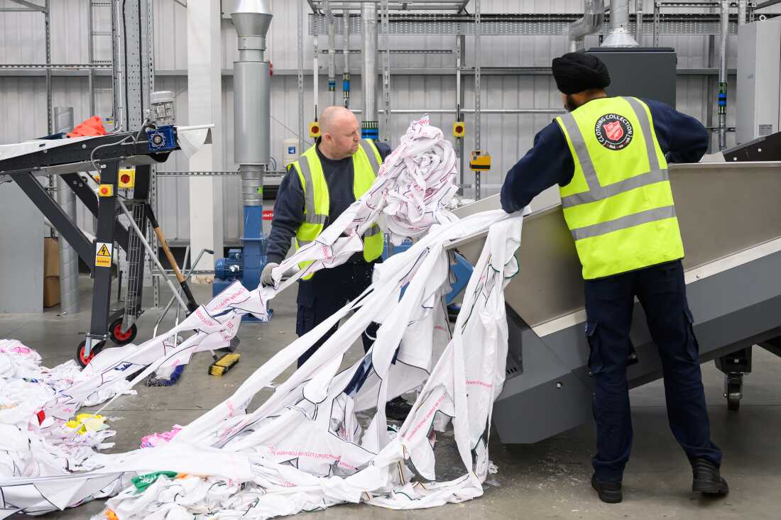 Two workers wearing yellow safety vests load unwanted polyester textiles into the Project Re:Claim system.