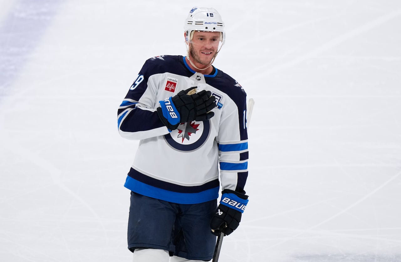 A hockey player smiles and puts his hand over his heart, tapping his chest as he skates.