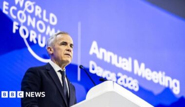 Donald Trump and Keir Starmer sit in a formal drawing room setting  on arm chairs with US and UK  flags behind them. Both have serious expressions and are looking out and not at each other.