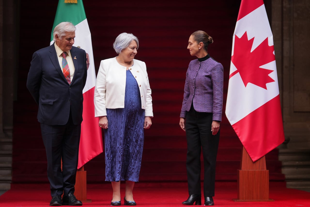 A man and two women stand next to the flags of Canada and Mexico.