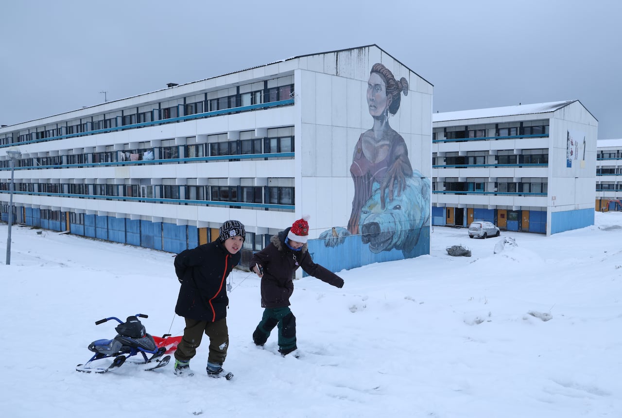 Two children with a sled next to a residential apartment building.