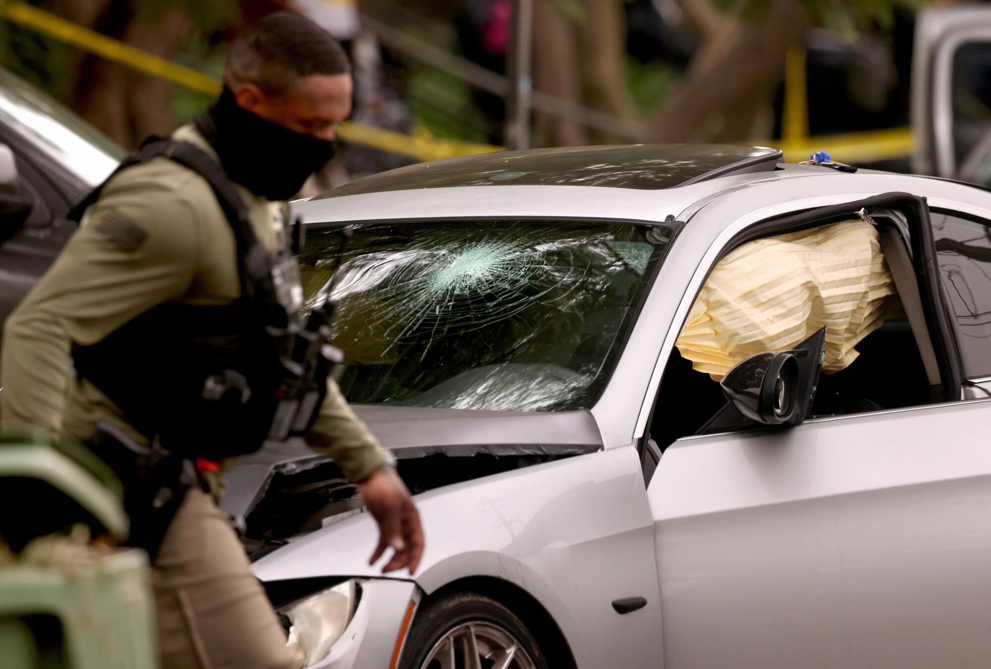 A federal agent walks past a bullet shattered window of a car involved in a shooting in Willowbrook.