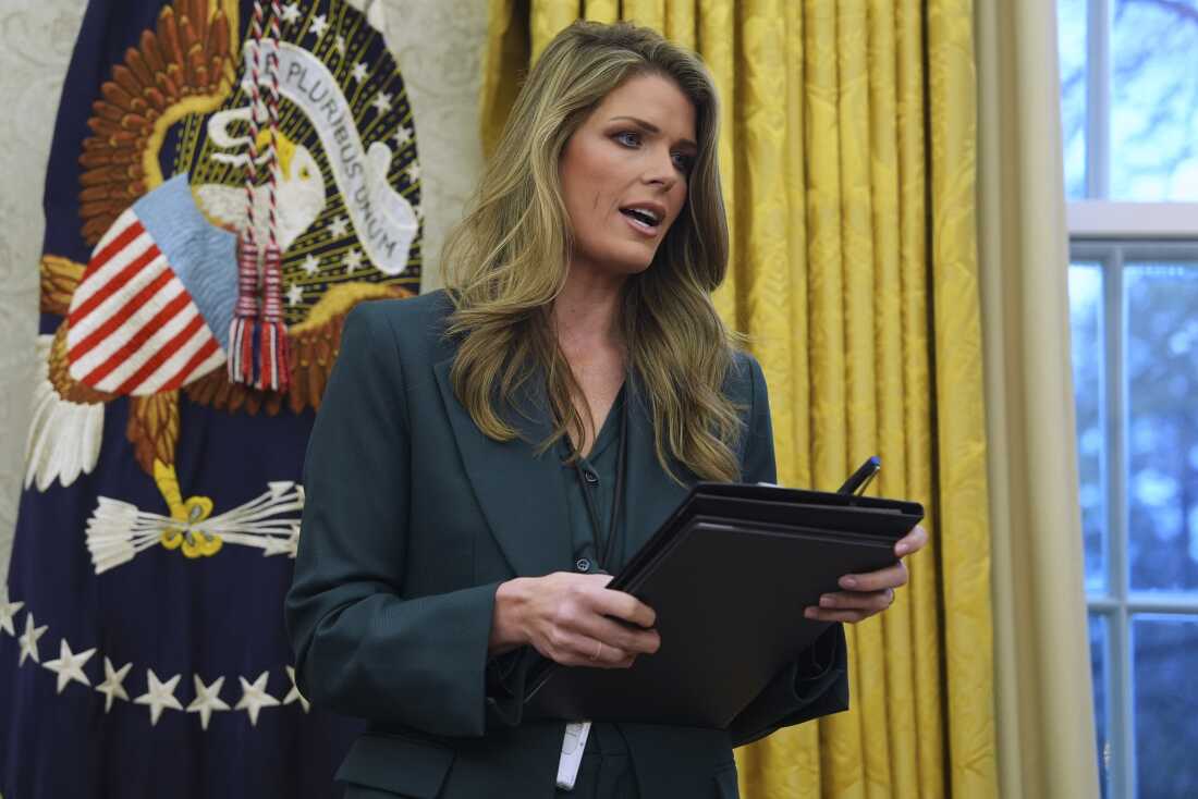Standing in the Oval Office on January 31, 2025, Lindsey Halligan speaks while holding a folio. Gold curtains and a flag with the U.S. president's seal are in the background.