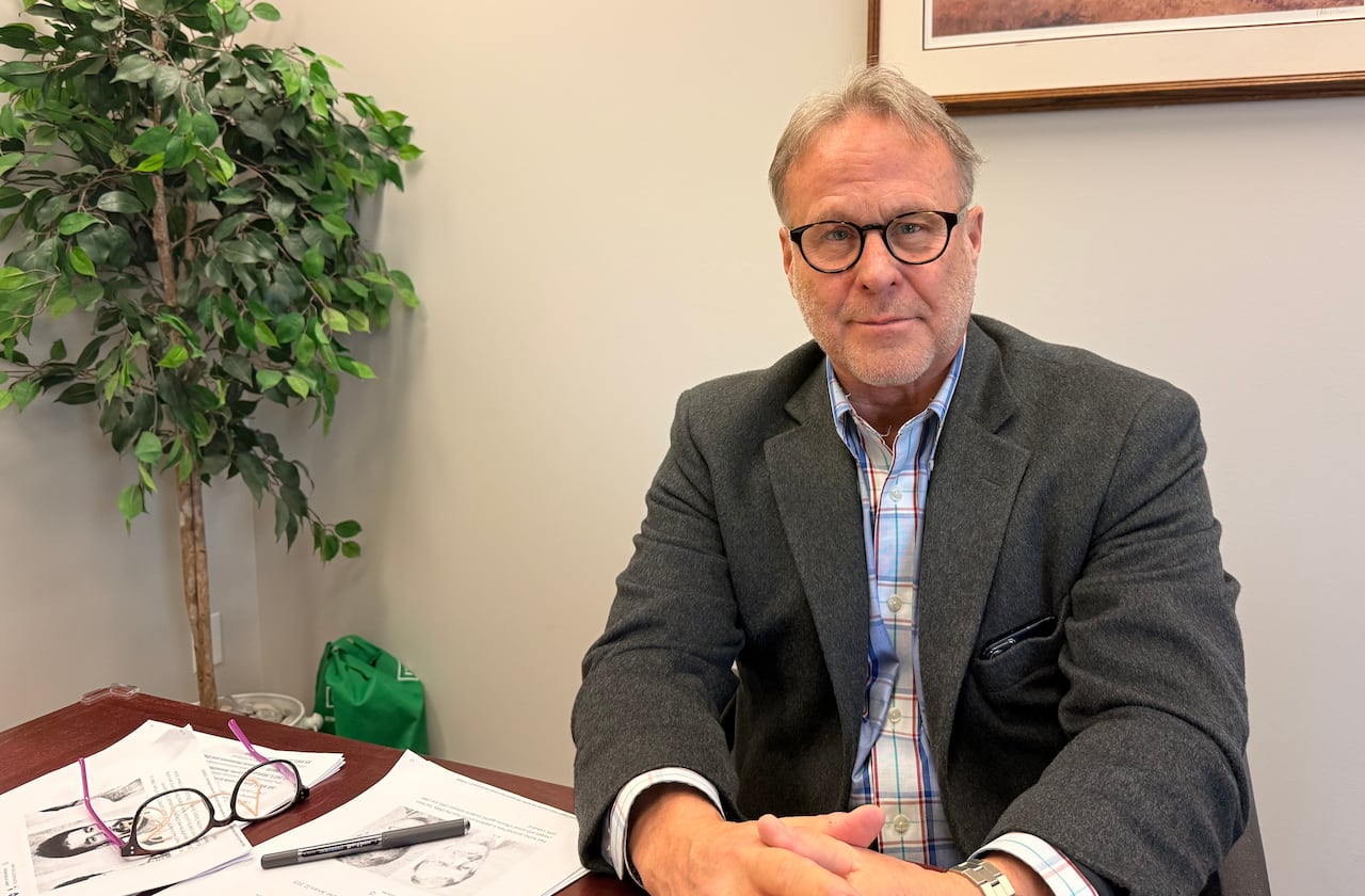 A man in glasses sits at a desk. 
