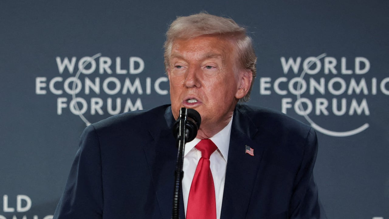 A man in a suit with a red tie speaks into a microphone.