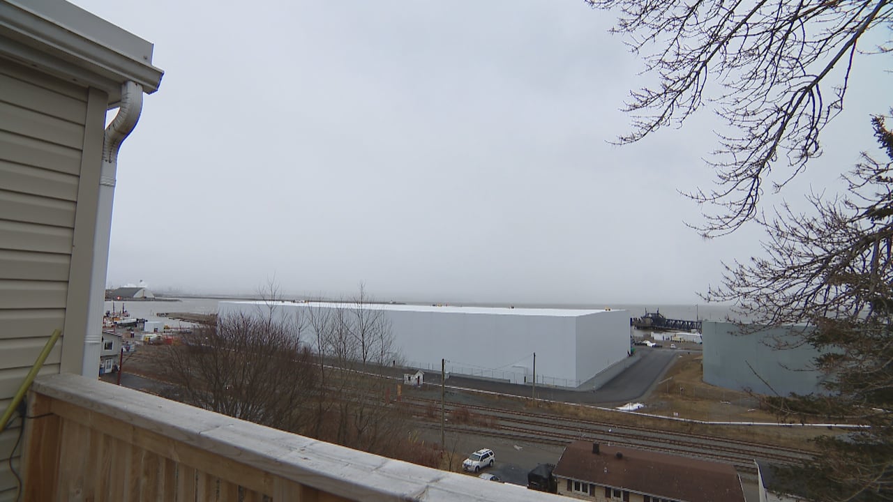 A view from a back deck, with the railing partially in view, of a waterfront with a large, rectangular white building in front of it. 