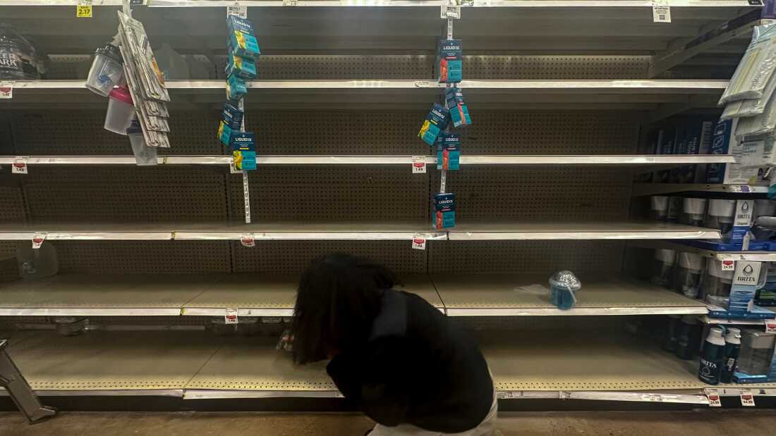 A shopper searches for water on near-empty shelves in a grocery store ahead of winter weather, Wednesday, in Marietta, Ga.