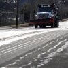A truck with a snowplow on the front applies salt brine to a road.