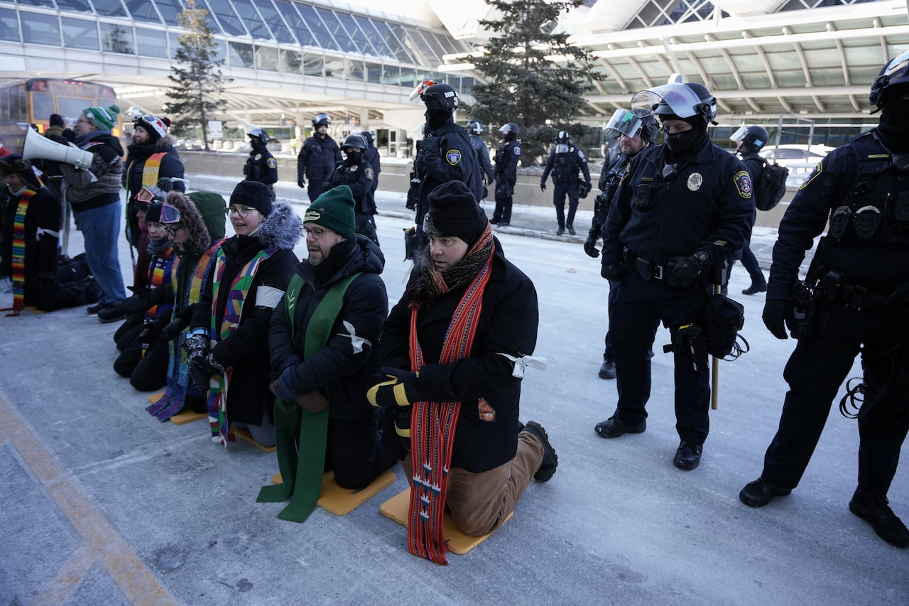 A group of clergy members kneel on the ground, in a line, during a protest in Minneapolis