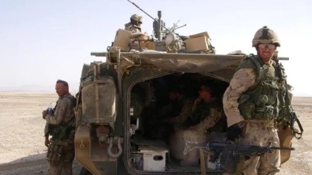 Several soldiers stand around a vehicle in a desert.