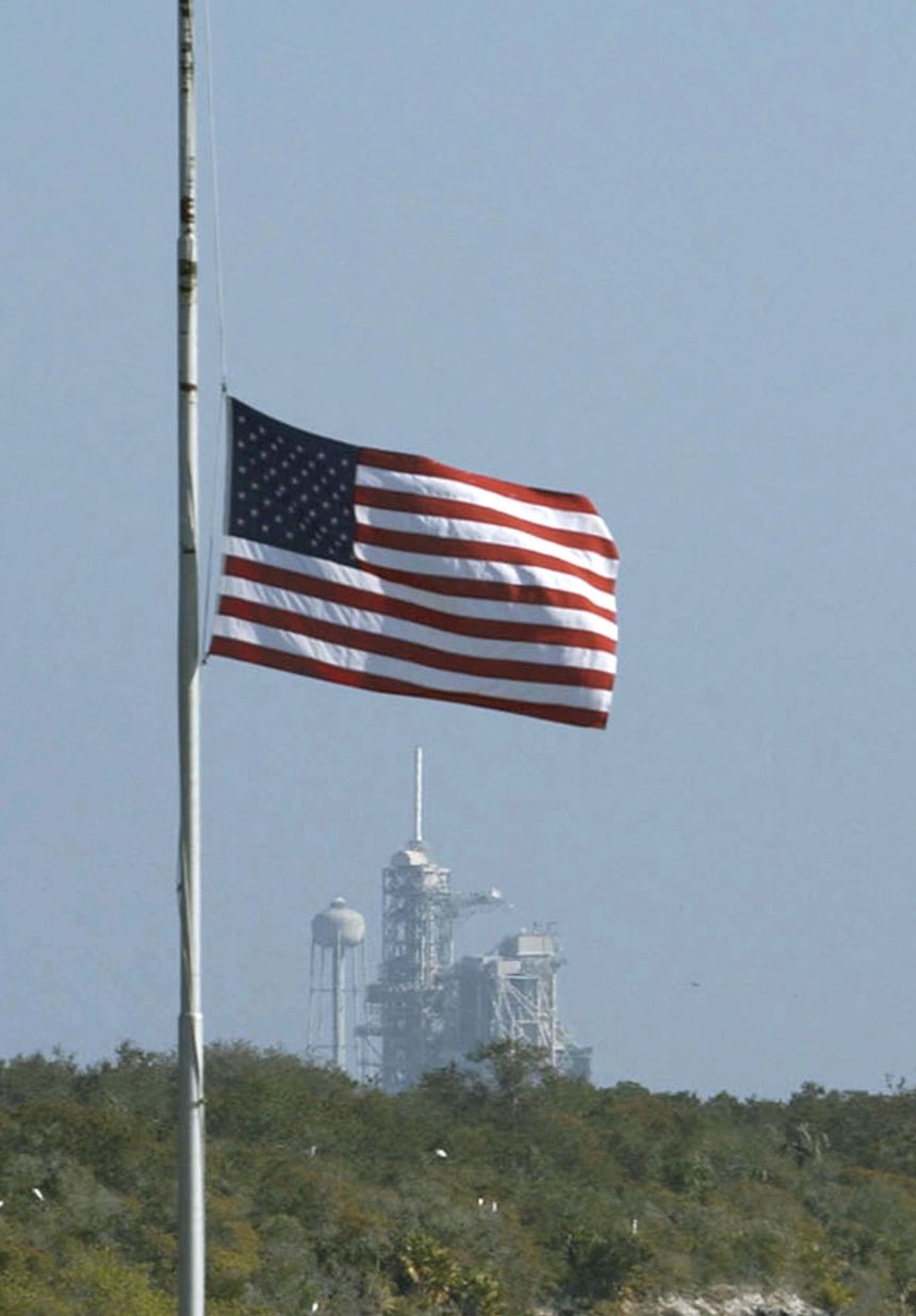 The American flag is lowered to half staff at the press site with launchpad 39A in the background, at Kennedy Space Center on February 1, 2003, following the Space Shuttle Columbia disaster.