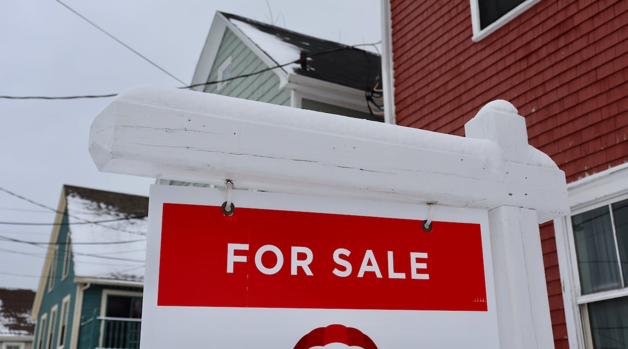 A 'for sale' sign outside a few properties with snow around.