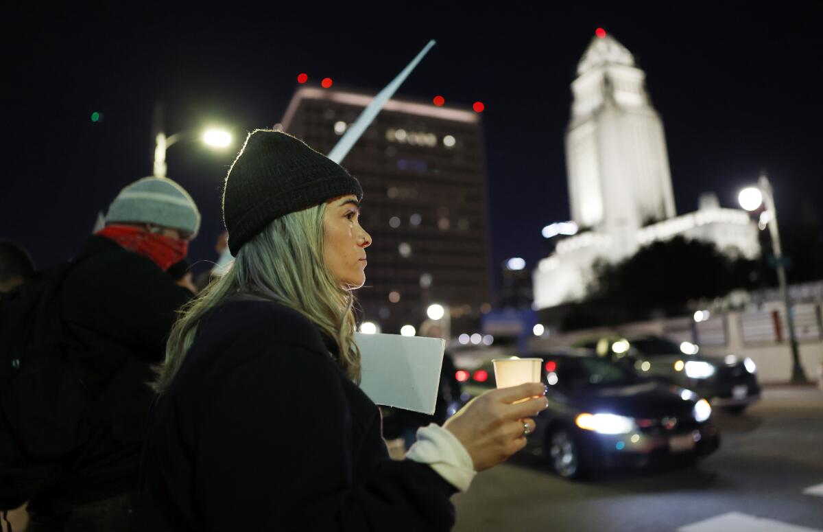 A woman participates in a candlelight vigil, with L.A. City Hall in the background.
