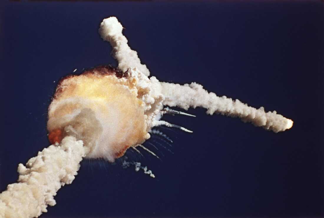 The space shuttle Challenger explodes shortly after lifting off from Kennedy Space Center in Florida on January 28, 1986. Against a deep-blue sky, debris radiates outward in plumes of smoke.