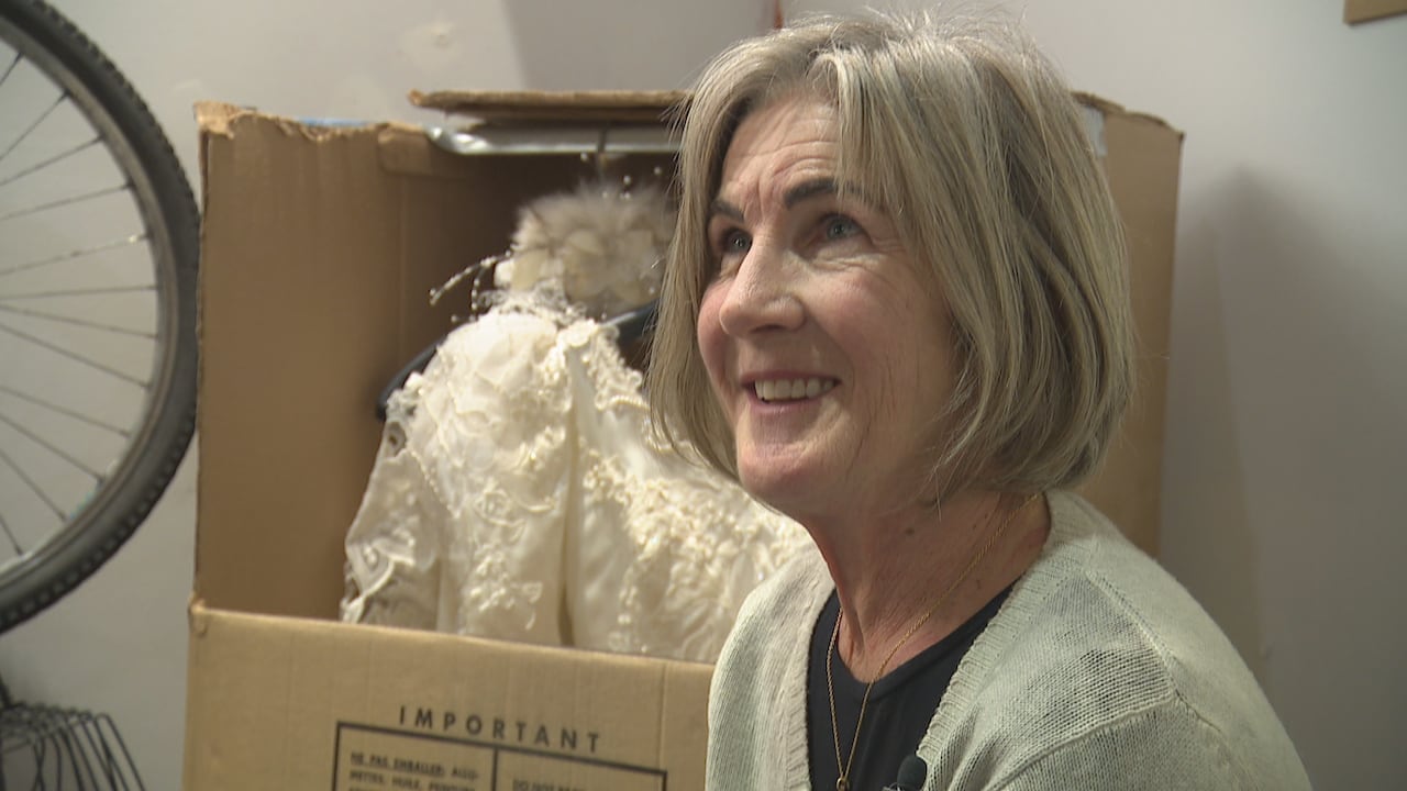A woman smiles in front of a box in which a wedding dress hangs