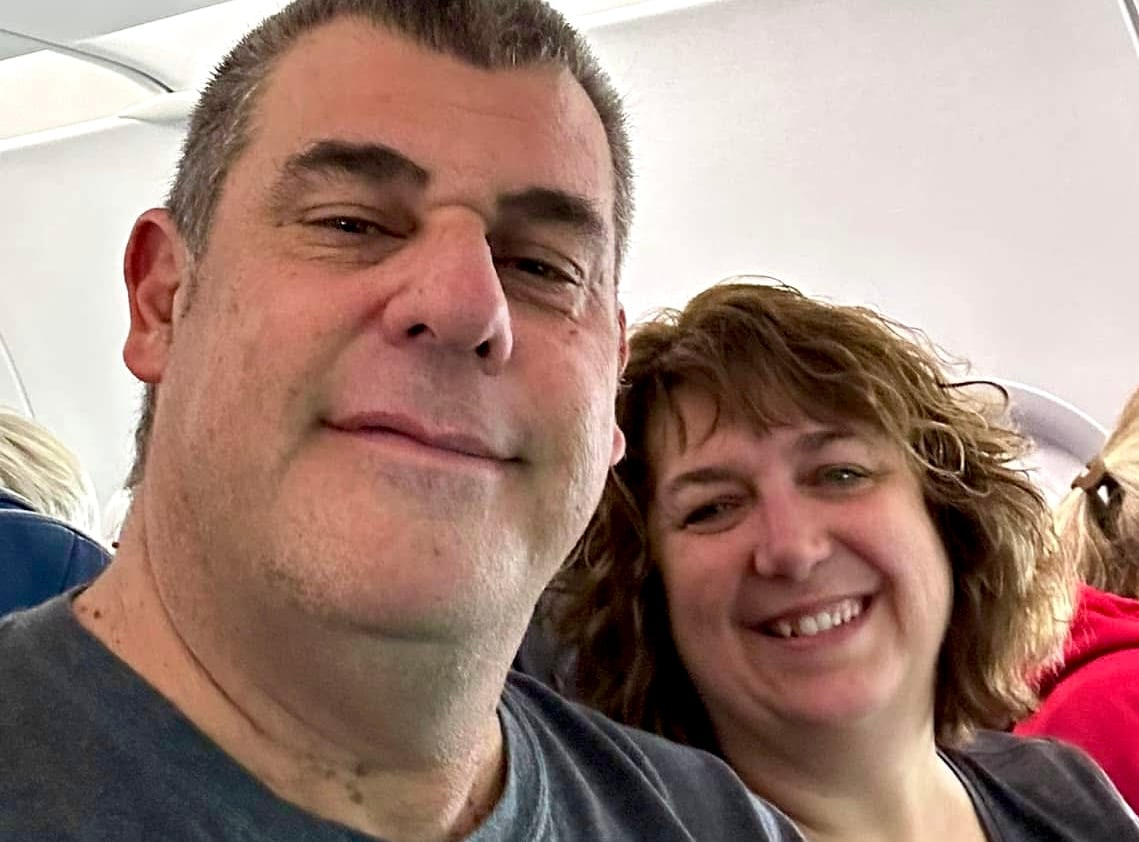 A man and a woman smile in a selfie-style photo on a plane.