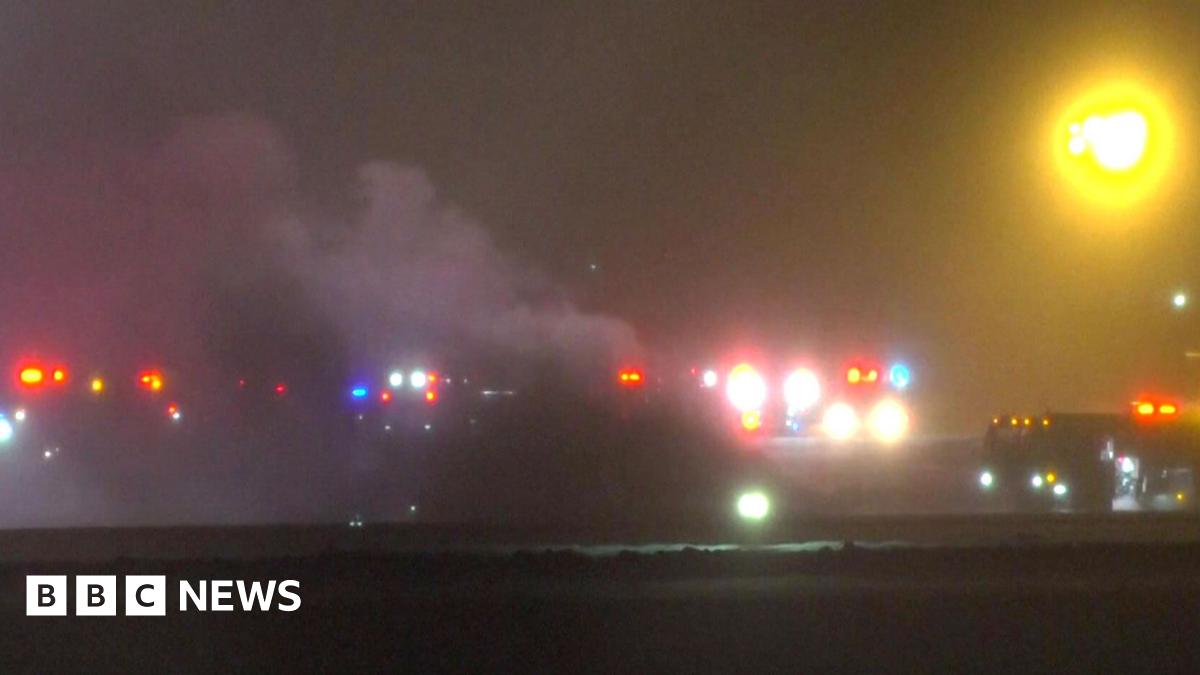 The blurry image shows the runway at Bangor Airport with smoke rising and red lights emanating from vehicles nearby