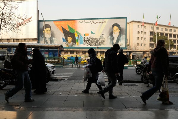 People walk in front of a mural depicting the late Iranian revolutionary founder Ayatollah Khomeini, right, members of the Basij paramilitary force and Supreme Leader Ayatollah Ali Khamenei along Enqelab-e-Eslami (Islamic Revolution) Street in Tehran, Iran, Sunday, Jan. 25, 2026. (AP Photo/Vahid Salemi)