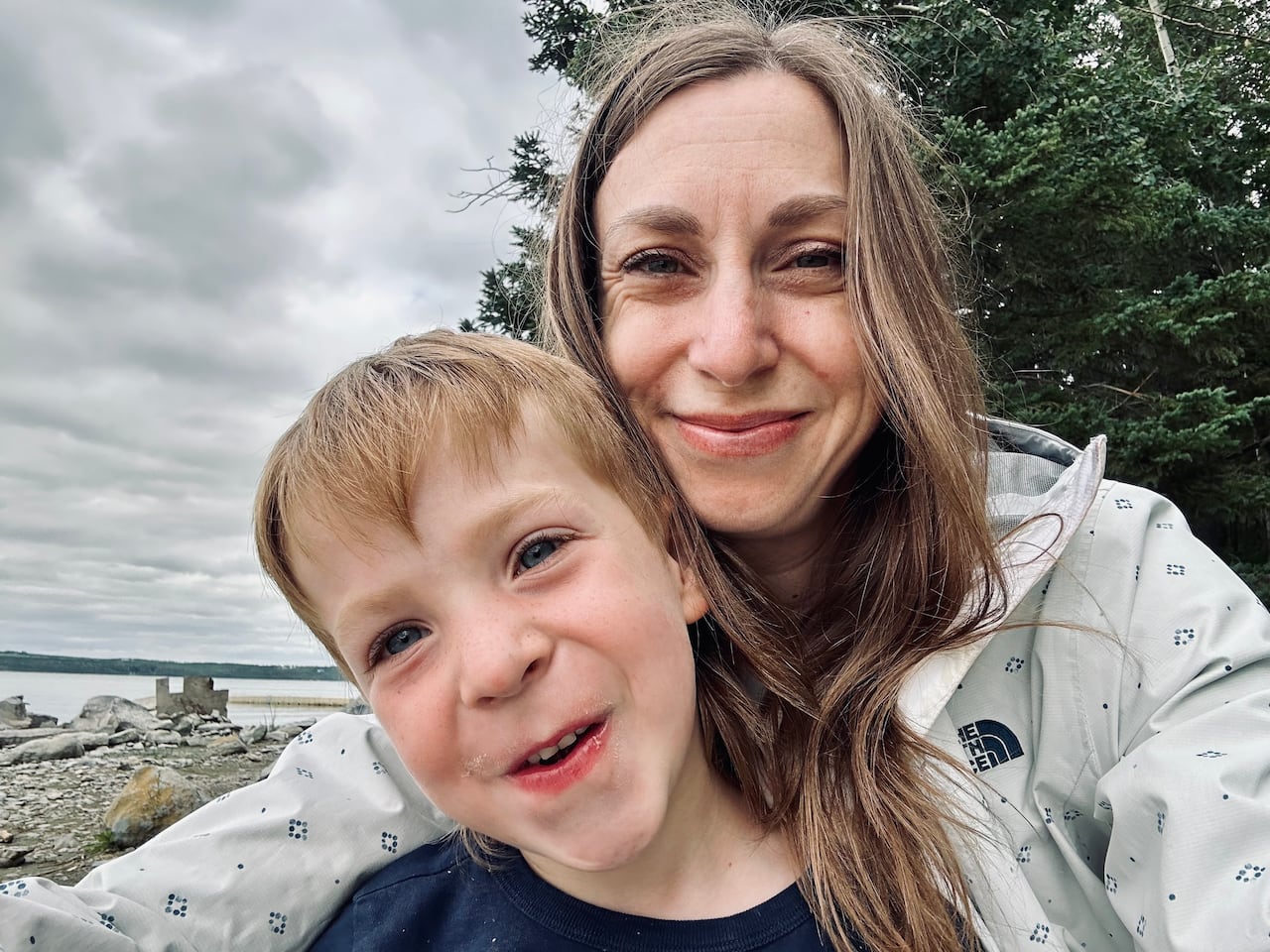 A woman takes a selfie with a young boy on a beach