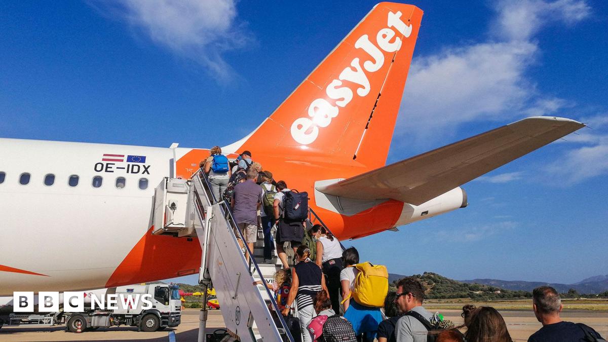 People boarding an EasyJet flight some carrying hand luggage and rucksacks on airport tarmac in Sardinia. It's a sunny day and the sky is blue.
